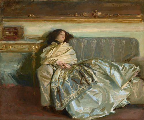 A woman in a luxurious, reflective gown reclines on a gray sofa. Her eyes are closed, conveying a serene or contemplative mood.